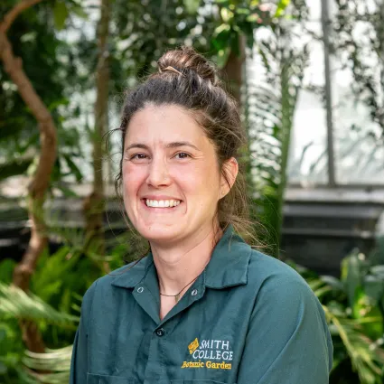 Woman with brown hair tied up in a green button down work shirt. 