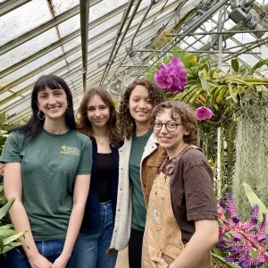 Four students posing for a photo next to pink orchids.