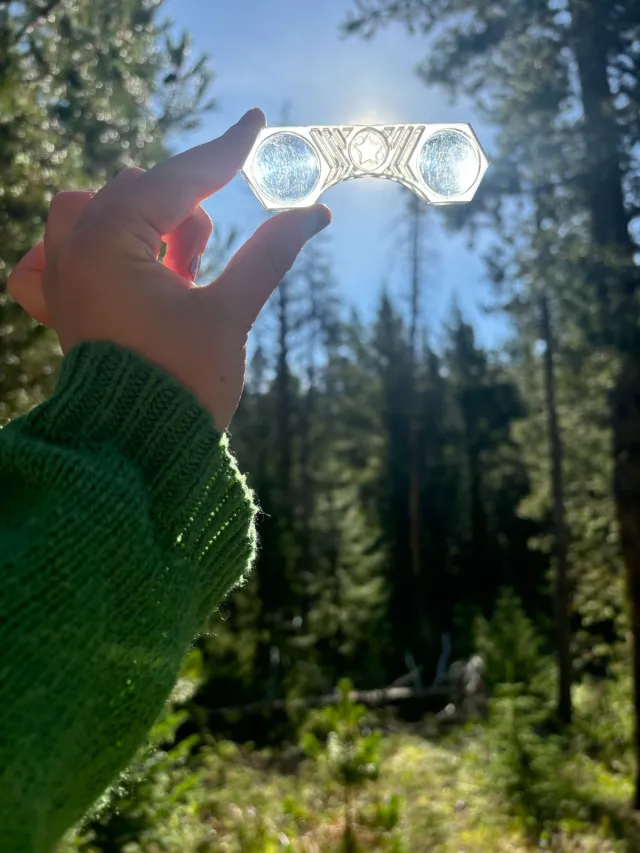 close up of binoculars with a hand holding them against the blue sky