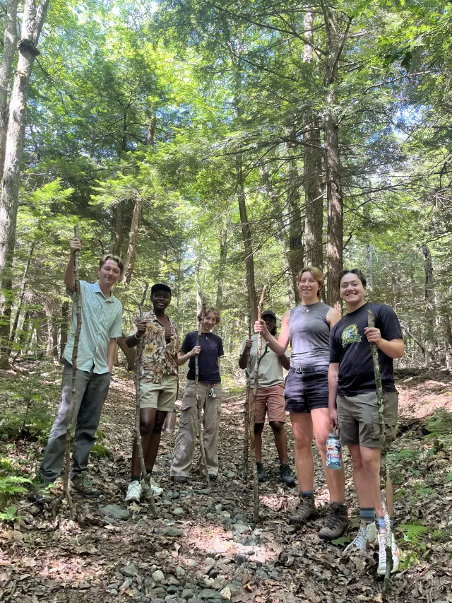 Group of college students in the woods holding walking sticks. 