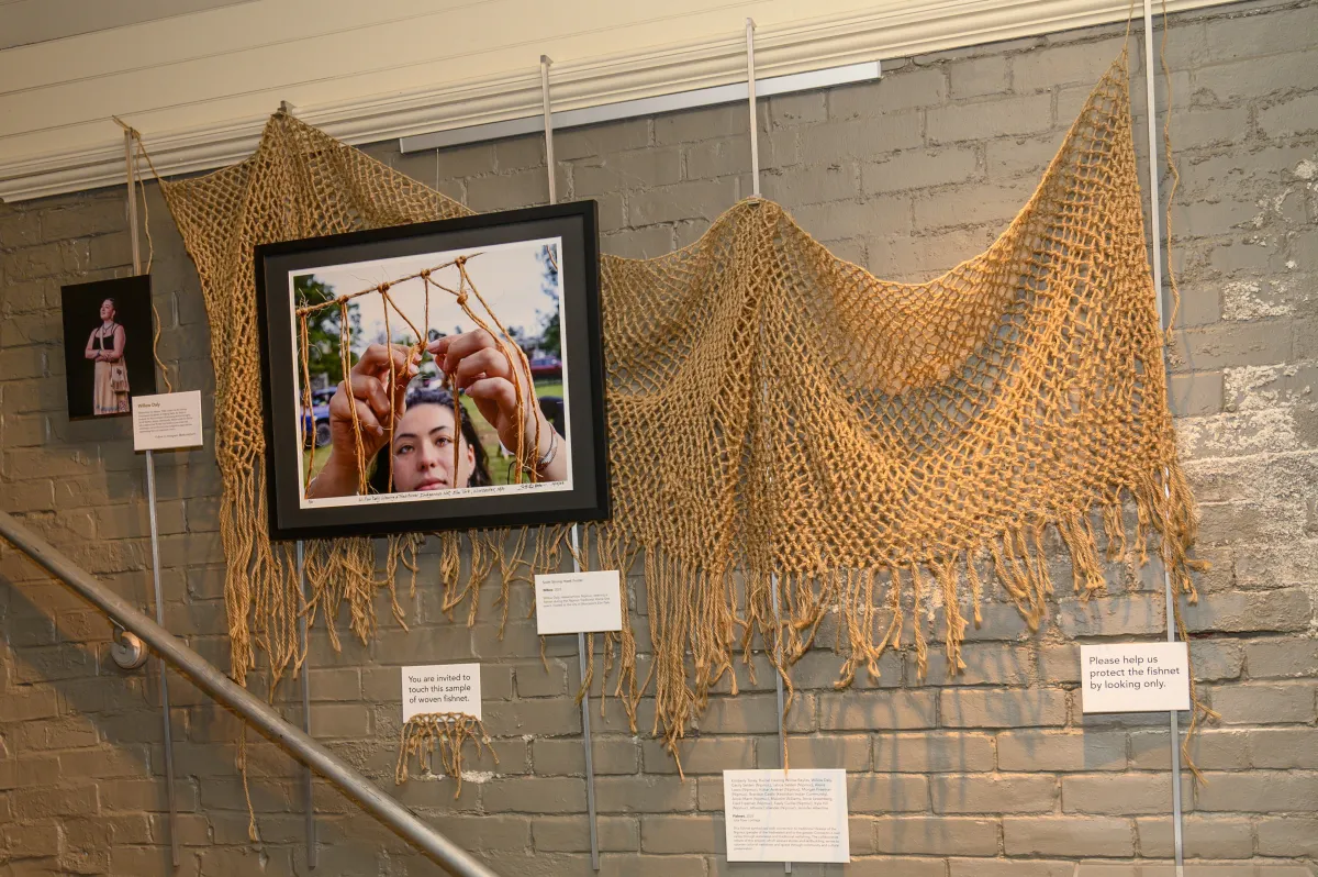 Fish net hung on gallery wall with photo of individual making the fishing net. 