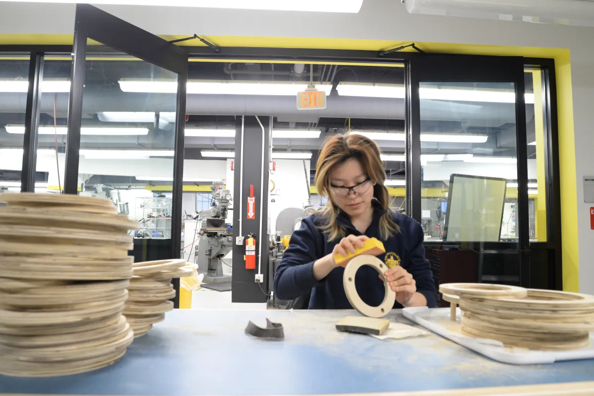 Woman sanding a round wooden ring with safety googles on.