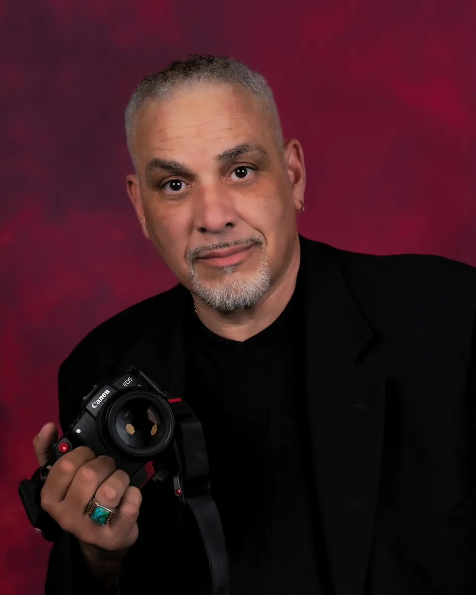 Man with short white hair holding a camera