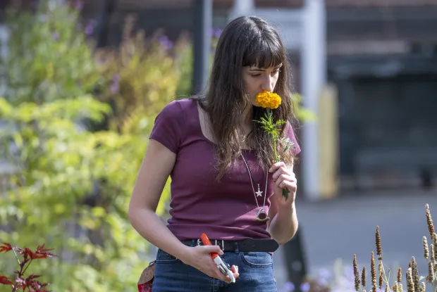 Student with long dark brown hair smelling a marigold. 